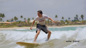 Aluno de surf em pé na prancha com palmeiras ao fundo em Porto de Galinhas